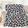 A leopard print flannel throw blanket featuring black, pink, and blue spots draped over a light-colored sofa.