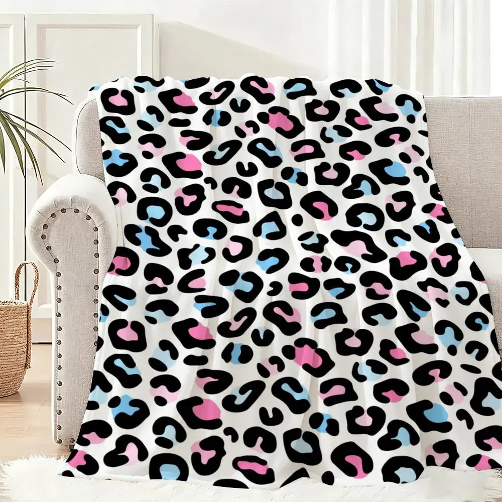 A leopard print flannel throw blanket featuring black, pink, and blue spots draped over a light-colored sofa.