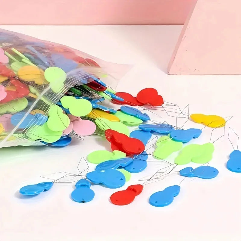 A pile of colorful plastic needle threaders in various shades of green, blue, and red scattered on a white surface.
