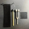 A black fabric pouch and a silver tuning fork set with an activator resting on a dark gray surface.