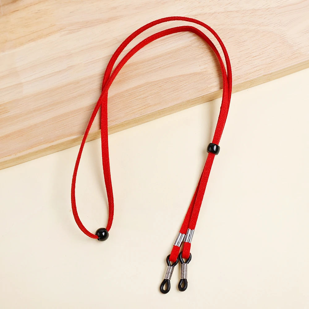 A red adjustable lanyard for glasses is displayed on a light wooden surface.