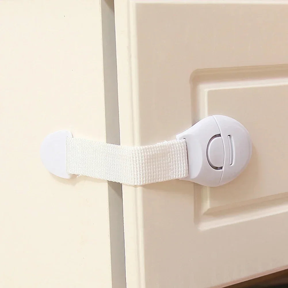 A white multi-purpose baby safety strap is attached to a cabinet door using a hook and strap.