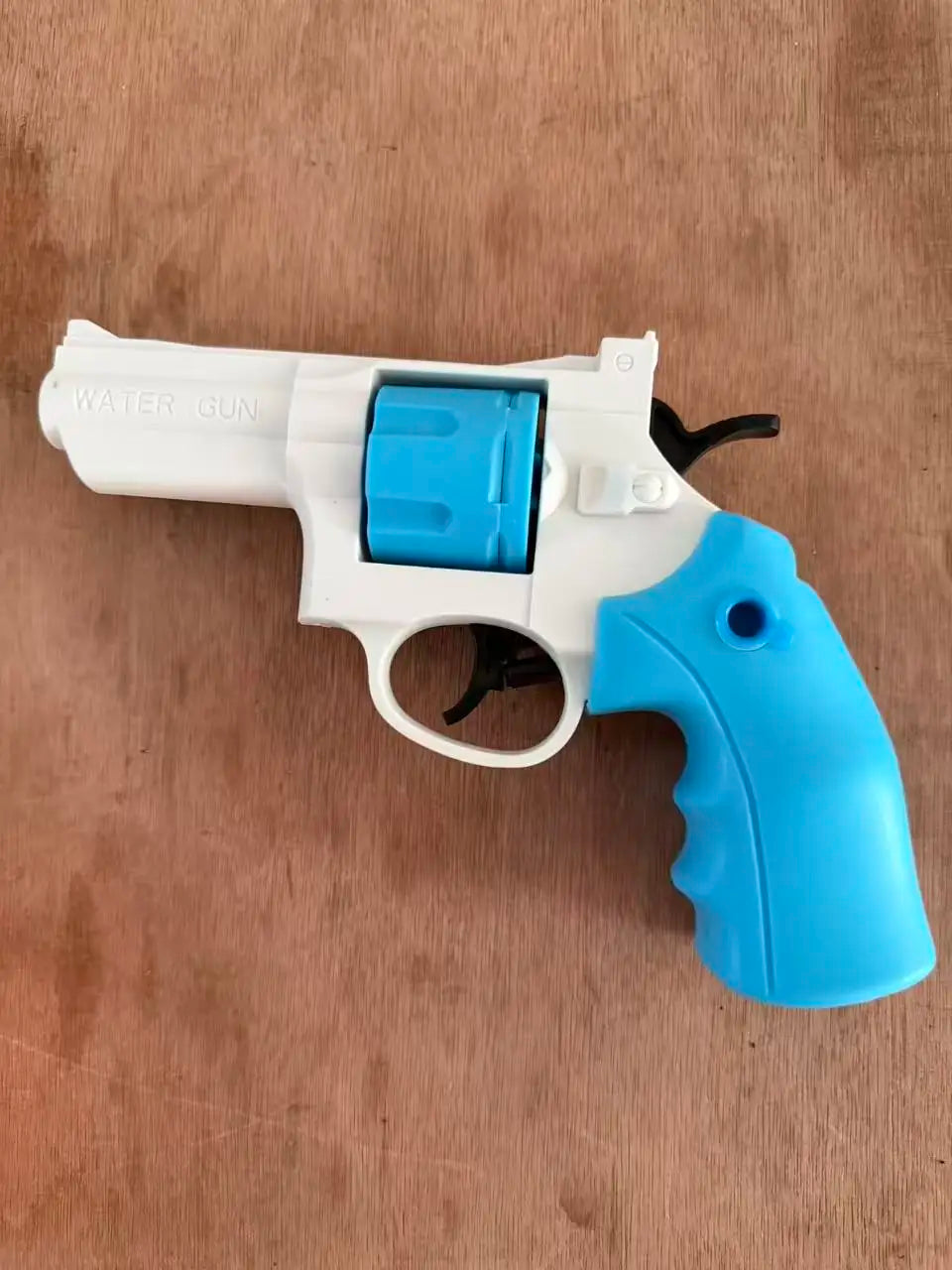 A white and blue mini mechanical revolver water gun is shown resting on a wooden surface.
