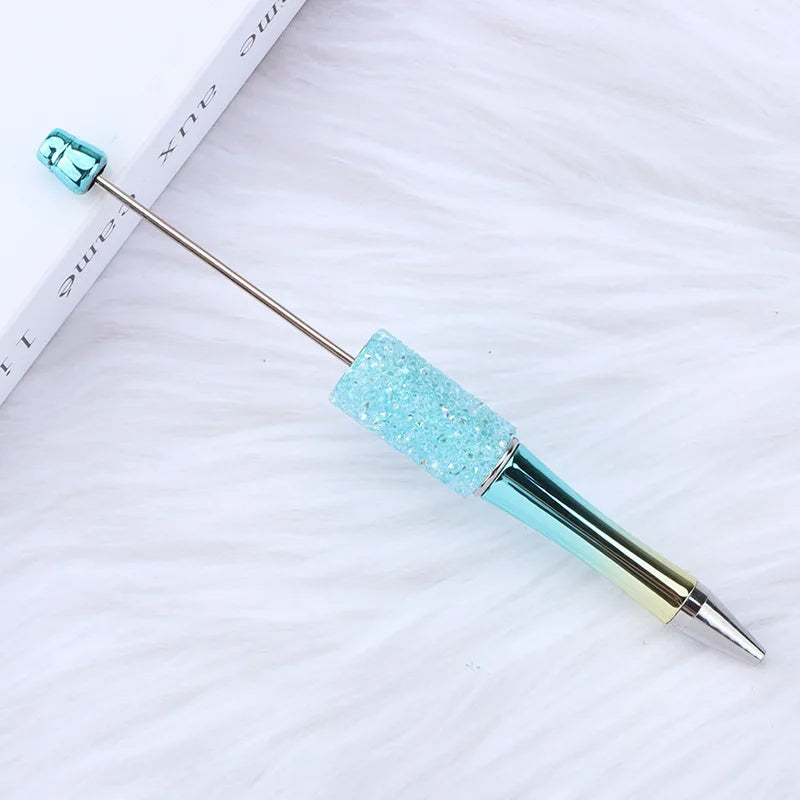 Un set de trente stylos-plumes en perles avec des accents turquoise et métalliques, exposés sur une surface blanche.