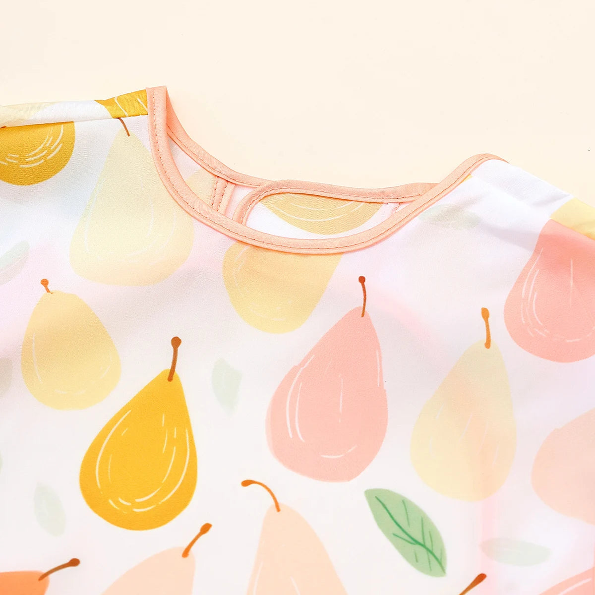 A close-up of a waterproof baby feeding bib with a sleeveless design featuring yellow and pink fruit patterns.