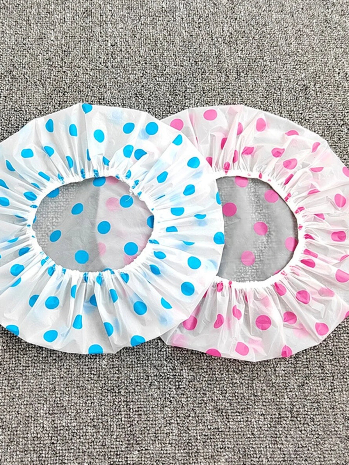 A pack of three disposable waterproof shower caps with polka dots in blue and pink on a gray background.