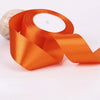 Orange satin ribbon roll unwrapped, showing the wide ribbon material and a white candle in the background.