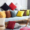 A collection of colorful velvet and corduroy cushions in shades of red, yellow, green, and gray arranged on a light blue sofa