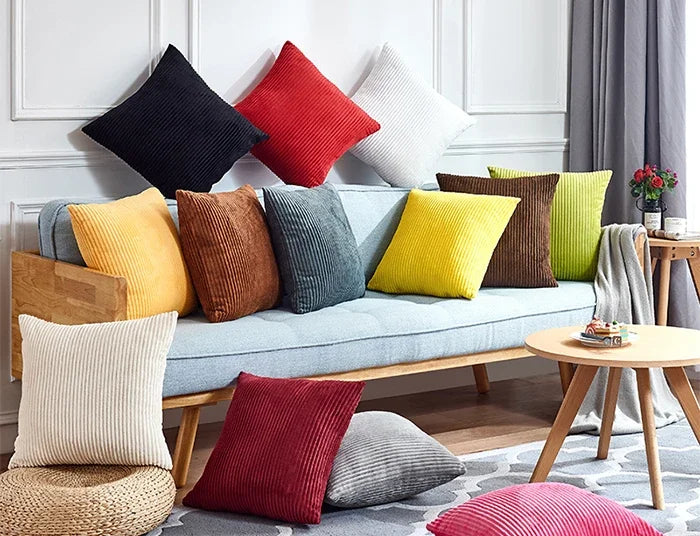A collection of colorful velvet and corduroy cushions in shades of red, yellow, green, and gray arranged on a light blue sofa