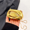 A hand holds a mini gold metal clutch bag with a yellow translucent top against a dark fabric background.
