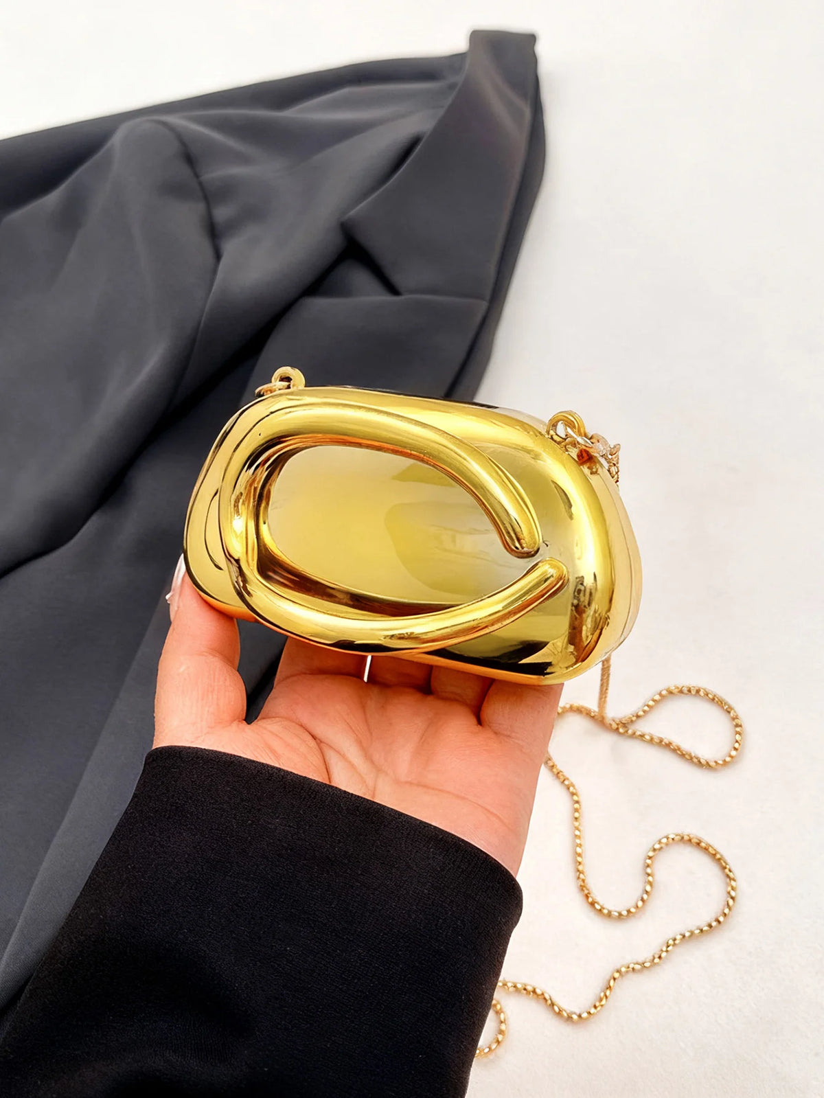 A hand holds a mini gold metal clutch bag with a yellow translucent top against a dark fabric background.
