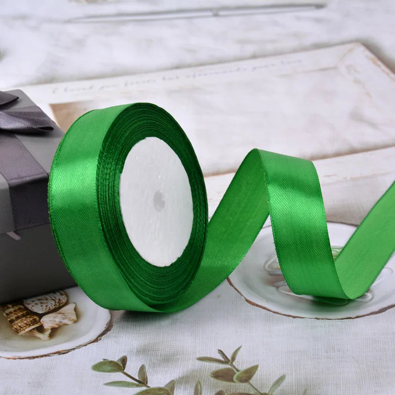 A roll of bright green lustrous satin ribbon lying on a white surface next to a small gift box.