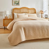 A beige plaid queen bedspread set with matching pillow shams displayed on a light wood bed frame.