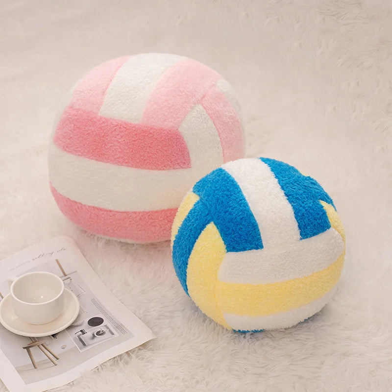A pink and white striped simulation volleyball plush toy resting on a white fluffy surface.