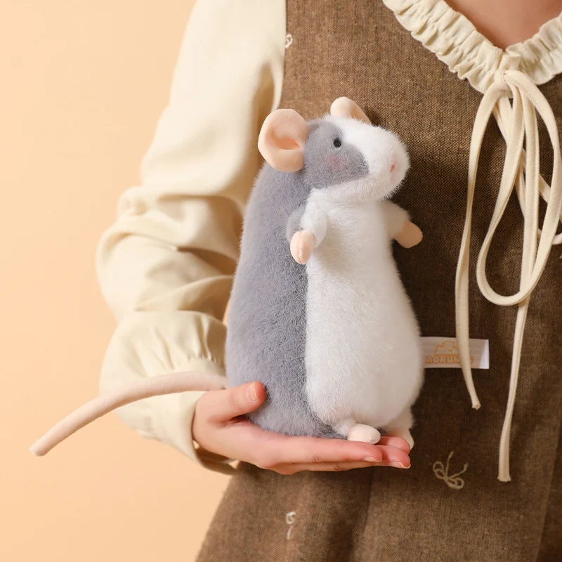 A small gray and white plush mouse stuffed animal being held by a person against a beige background.