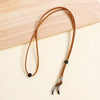 A brown leather lanyard with a metal clasp is laid on a light wooden surface.