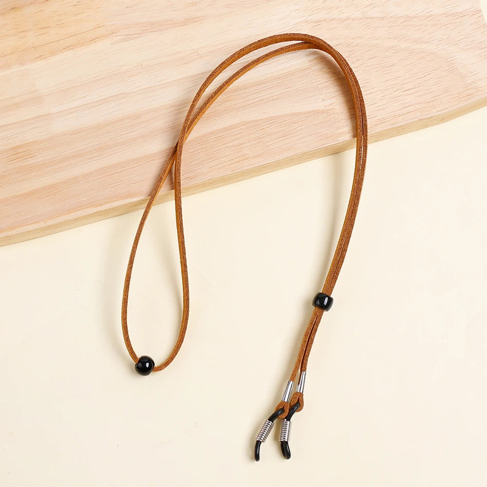 A brown leather lanyard with a metal clasp is laid on a light wooden surface.