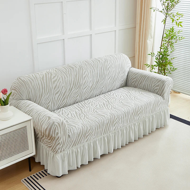 A light gray jacquard sofa cover with a wavy pattern and an elastic ruffle skirt displayed indoors.