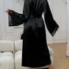 A black silk satin robe with lace trim is shown on a model in a bright room.