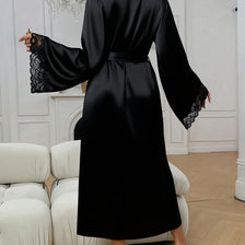A black silk satin robe with lace trim is shown on a model in a bright room.