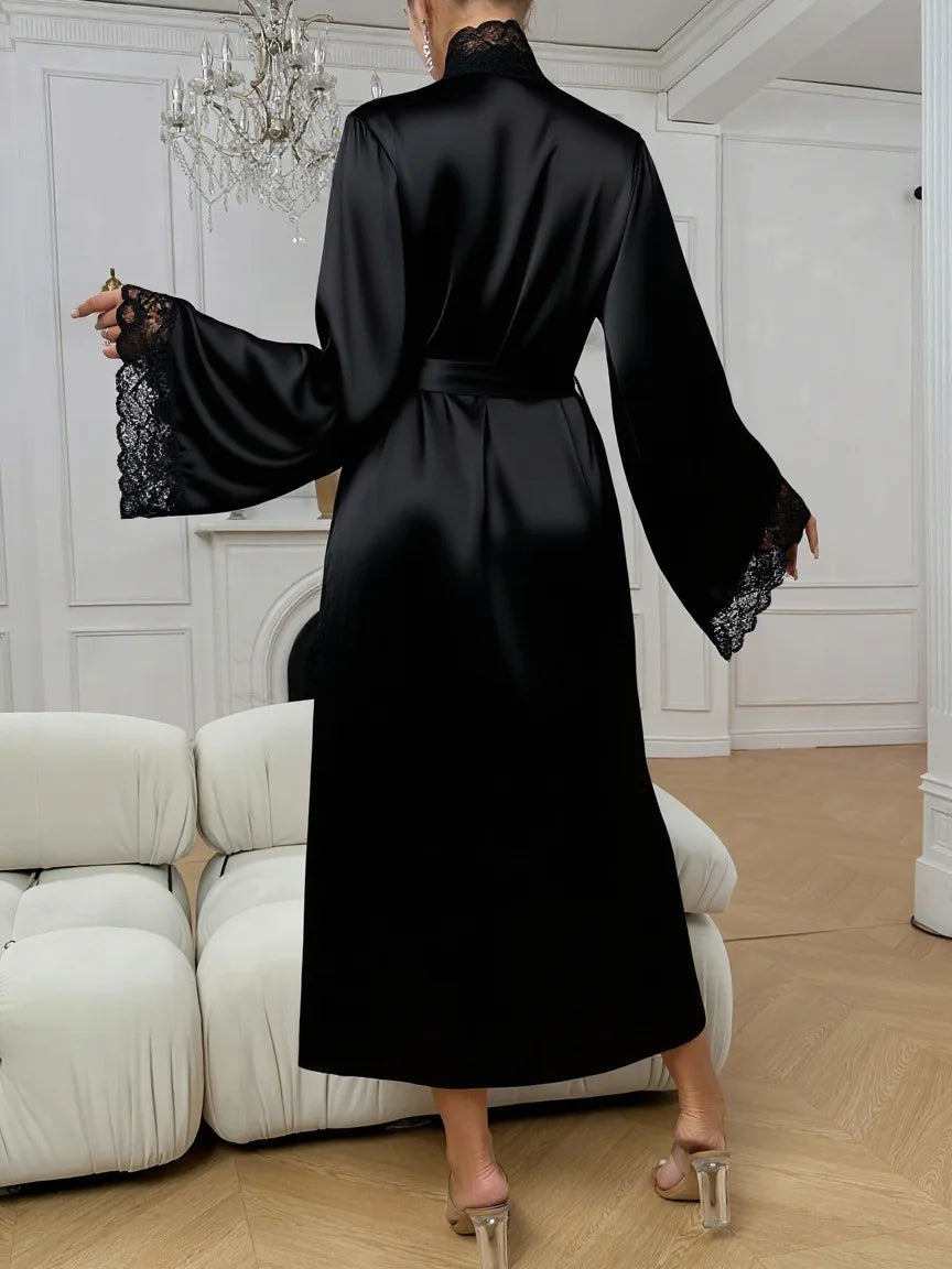 A black silk satin robe with lace trim is shown on a model in a bright room.