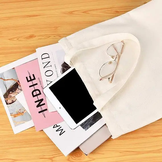 A canvas tote bag with a light beige lining and a pair of eyeglasses resting inside, placed on a wooden surface.