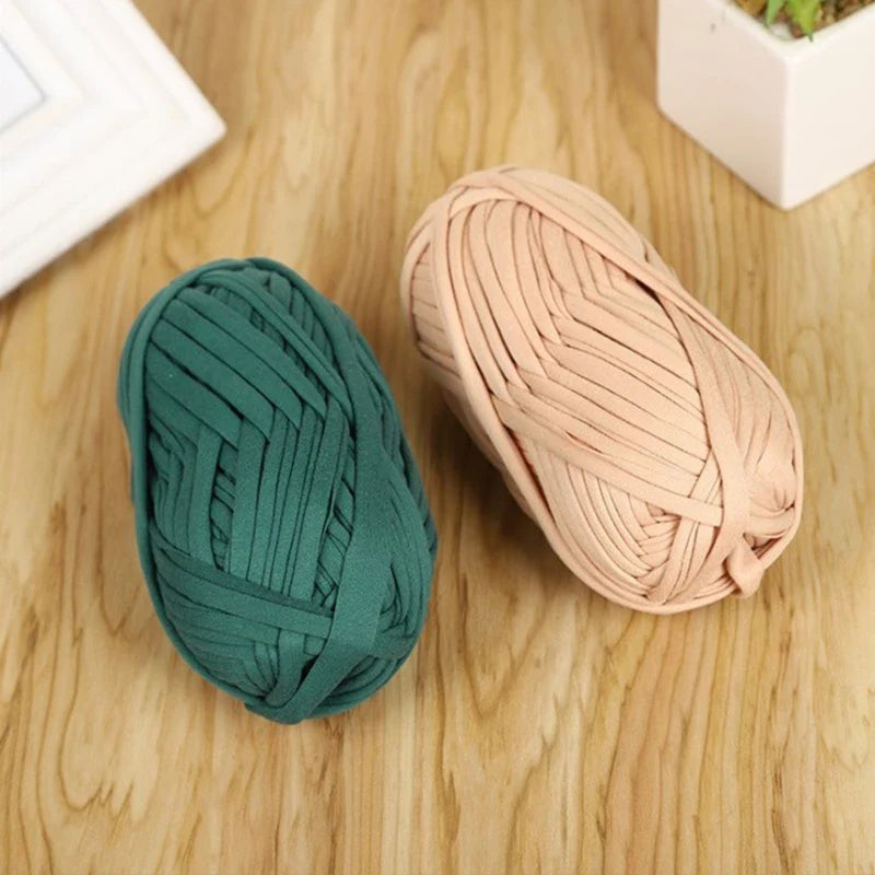 A ball of dark green soft T-shirt yarn for crochet and knitting resting on a wooden surface.