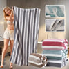 A woman models a set of gray and white striped microfiber bath towels in a modern bathroom setting.