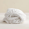 A rolled white linen fitted sheet with deep pockets is shown on a light surface.