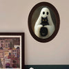 An oval framed picture featuring a ghost with white drapery and a black cat sitting on its chest.
