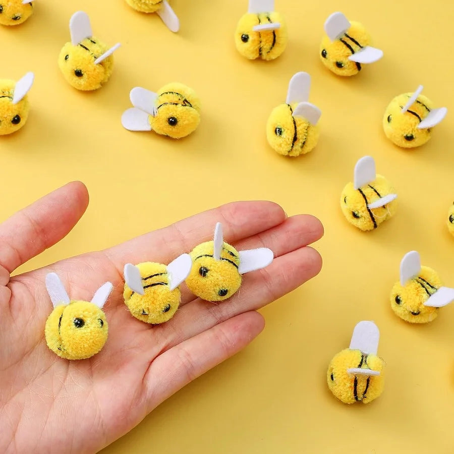 A hand holds a wool felt bee pompom decoration, surrounded by many similar yellow bee decorations.