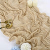 A beige cotton gauze table runner with ruffled folds, topped with white candles and floral accents.
