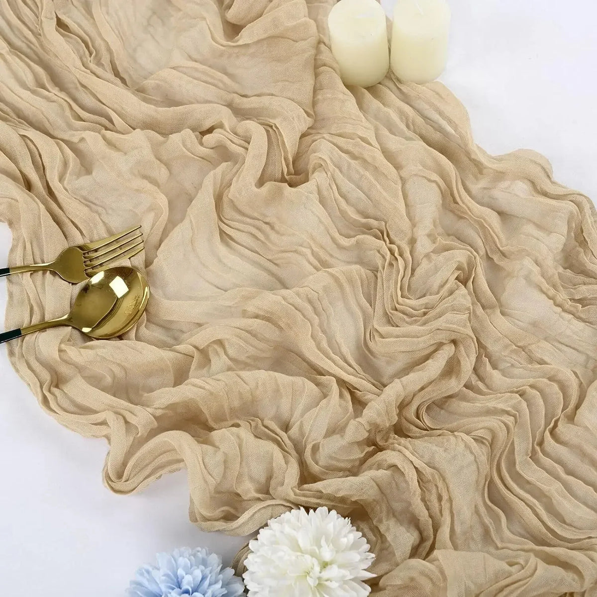 A beige cotton gauze table runner with ruffled folds, topped with white candles and floral accents.