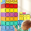 A young child is building a tower with colorful magnetic sheet building blocks on a light-colored surface.