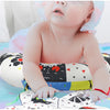 A baby is lying on a colorful mat, holding a high contrast tummy time pillow.