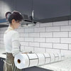 A woman is applying a roll of white self-adhesive kitchen splashback sticker to a tiled wall in a modern kitchen.