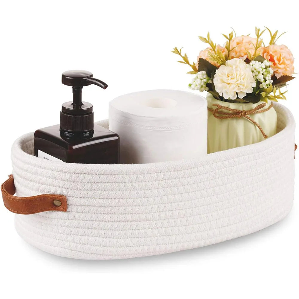 A woven cotton rope storage basket holding a white toilet paper roll and a small floral arrangement.
