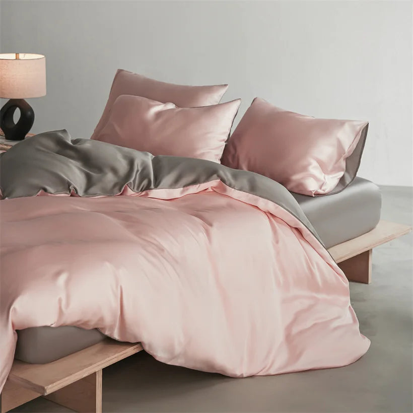 A luxury mulberry silk duvet cover set in soft pink and gray tones on a bed.