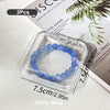 A clear jewelry organizer box containing three blue beads, shown next to a plant informational page.