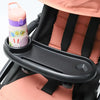 A pink and purple 3-in-1 stroller snack tray with a cup holder and phone slot is shown attached to a black stroller seat.