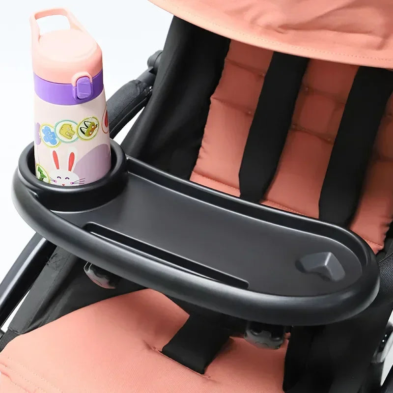 A pink and purple 3-in-1 stroller snack tray with a cup holder and phone slot is shown attached to a black stroller seat.