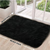 A rectangular black plush silk-touch area rug placed on a light wood floor near a glass door.