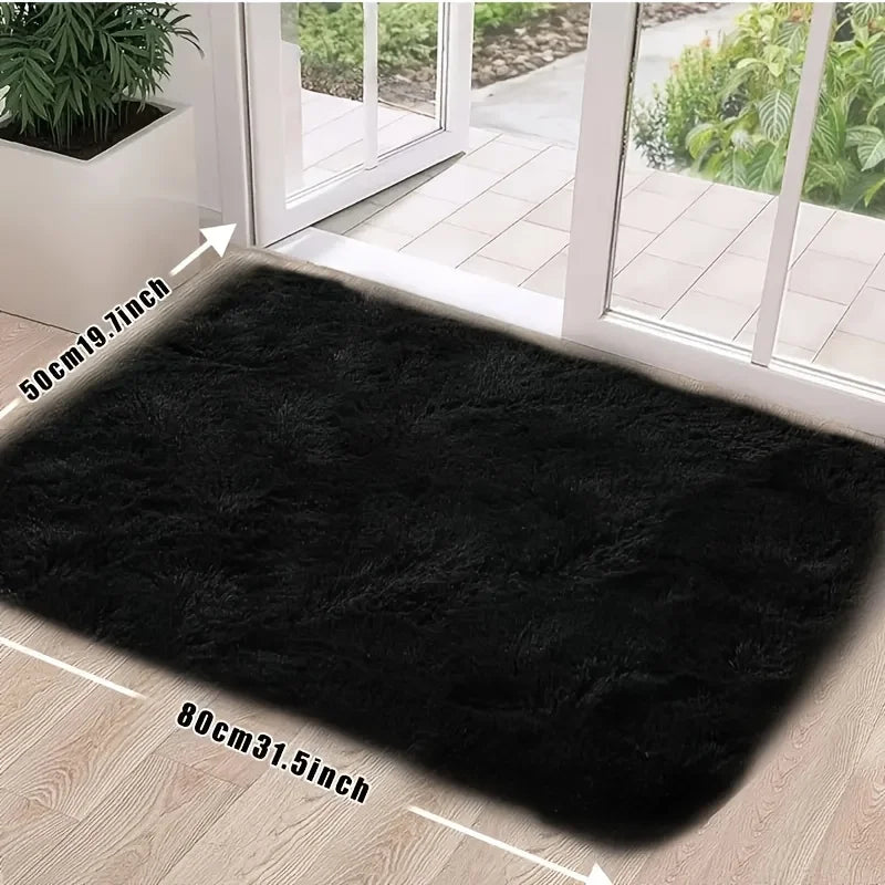 A rectangular black plush silk-touch area rug placed on a light wood floor near a glass door.