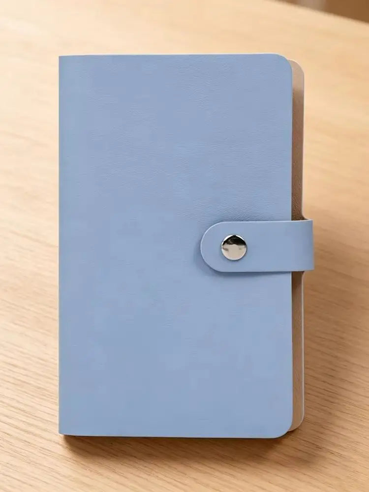 A light blue 100-slot cash organizer binder with a snap closure and transparent pages resting on a wooden surface.
