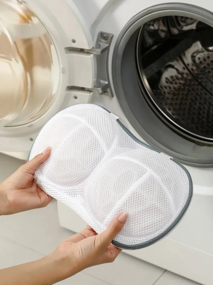 Hands hold a white mesh laundry bag with anti-deformation protection inside a washing machine drum.