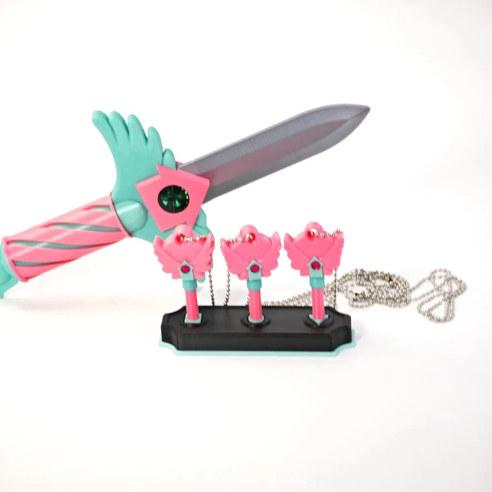 A set of four pink and teal dagger key necklaces displayed on a black base.