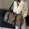 A person is holding a leopard print weekender tote bag with a black strap and shoe compartment.
