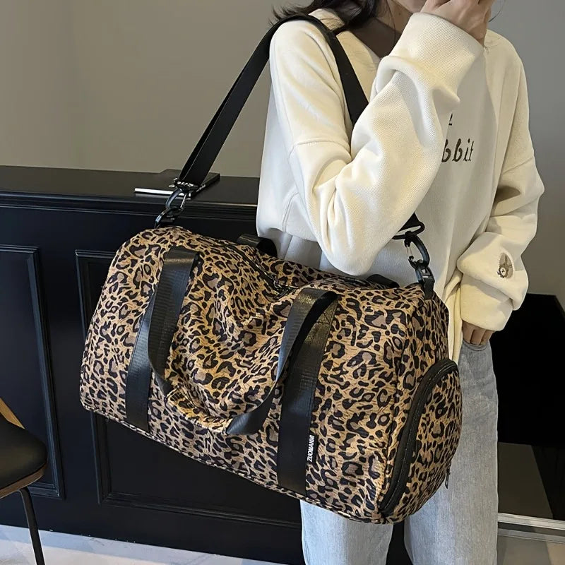 A person is holding a leopard print weekender tote bag with a black strap and shoe compartment.
