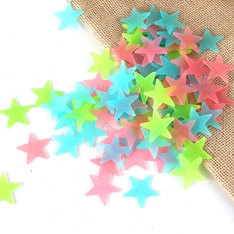 A pile of 100 luminous star-shaped wall stickers in various pastel colors like pink, blue, and green on a burlap background.