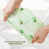 A hand holds a light green, tear-resistant tote bag featuring avocado print designs.